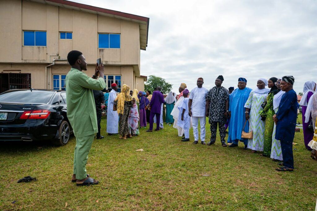 An outdoor Nigerian gathering with a speaker addressing the group, evoking oral tradition and shared wisdom